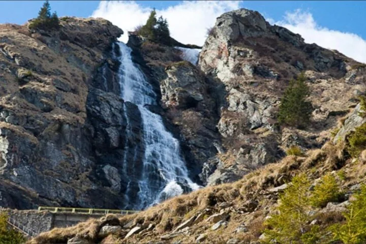 Una cascata che scende lungo un fianco roccioso della montagna con vegetazione rada.