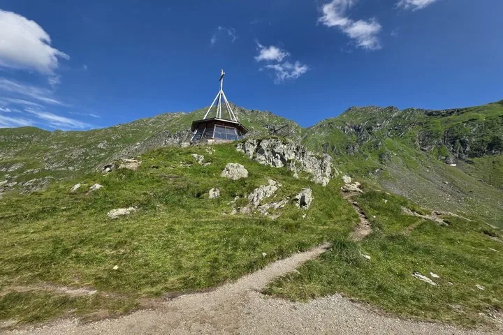 A small shelter with a cross on top of a grassy mountain.