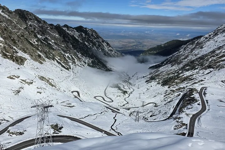 Snowy mountain landscape with the winding Transfagarasan road partially obscured by clouds.